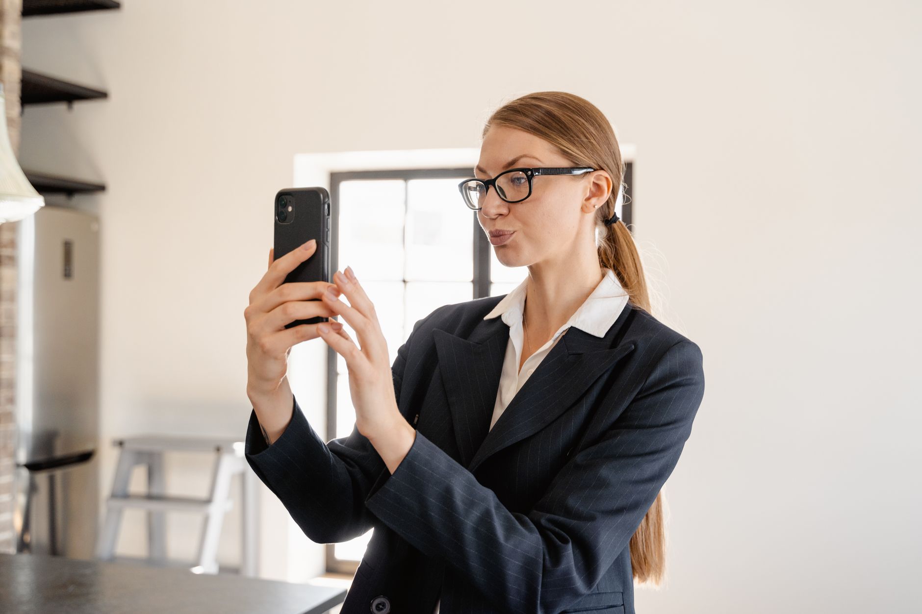 Authentic, user-snapped phone selfie of a professional in their real work environment (home office or agency floor). Imperfect angle, natural lighting, not a polished stock headshot.