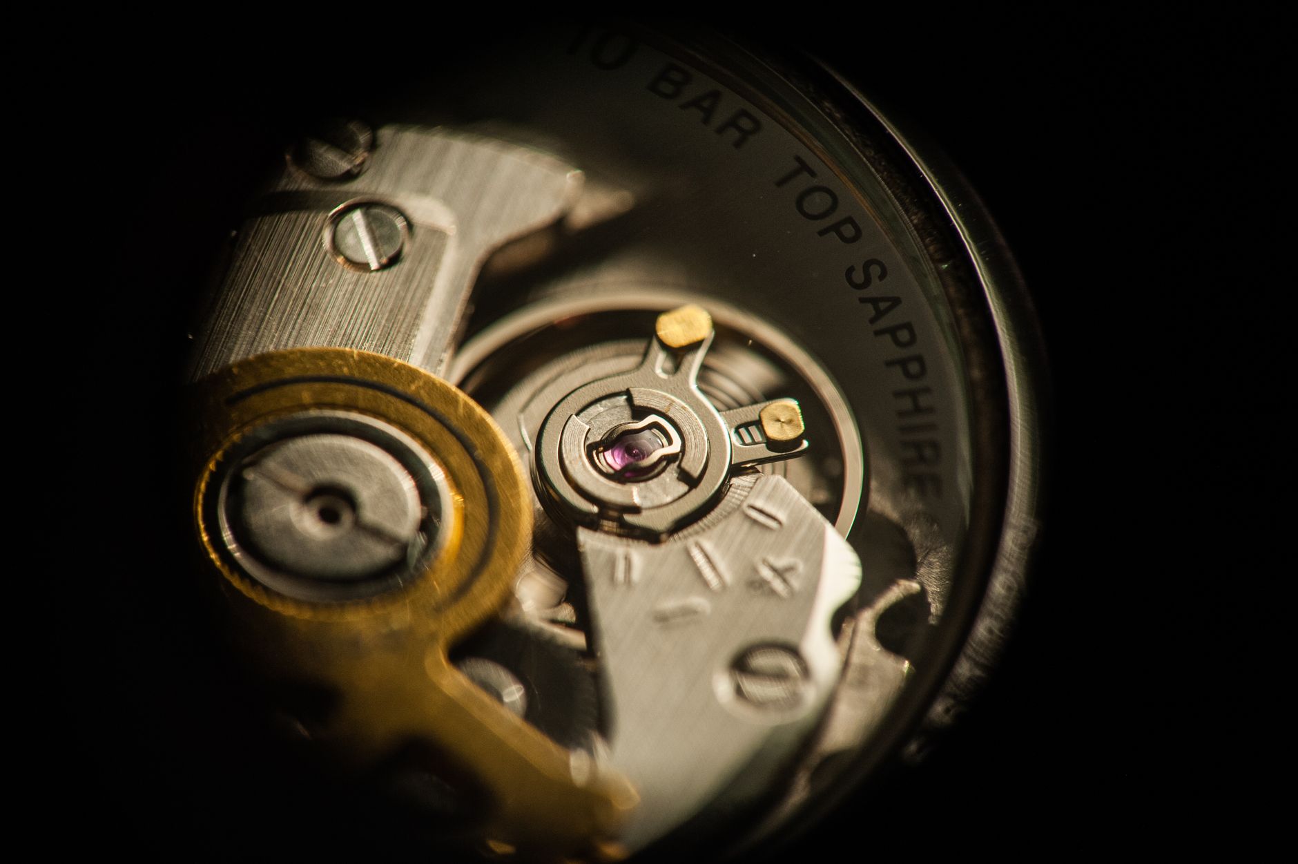 Close-up of a mechanical Swiss watch movement exposed on a dark oak desk, brushed steel gears interlocking, symbolizing precise automated systems. Morning light from a north-facing window. No people, no human figures. Not a generic robot illustration, not a glowing AI brain.